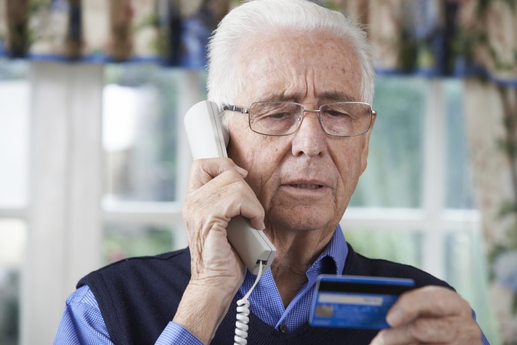 Protect Yourself from Scams as a Senior - Older adult man on the phone and looking at his credit card