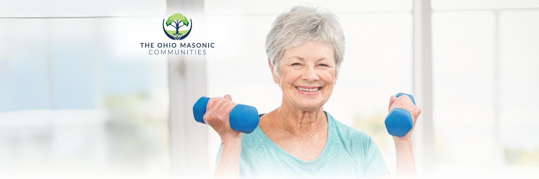 senior woman wearing an aqua shirt smiling while lifting two blue dumbbells while working out at a senior living community