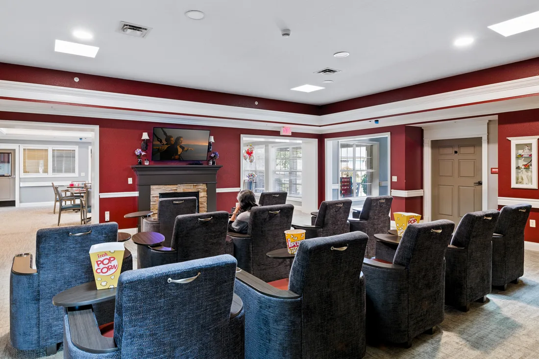 Memory support movie theater room with rows of chairs, popcorn, and a fireplace with a television above it