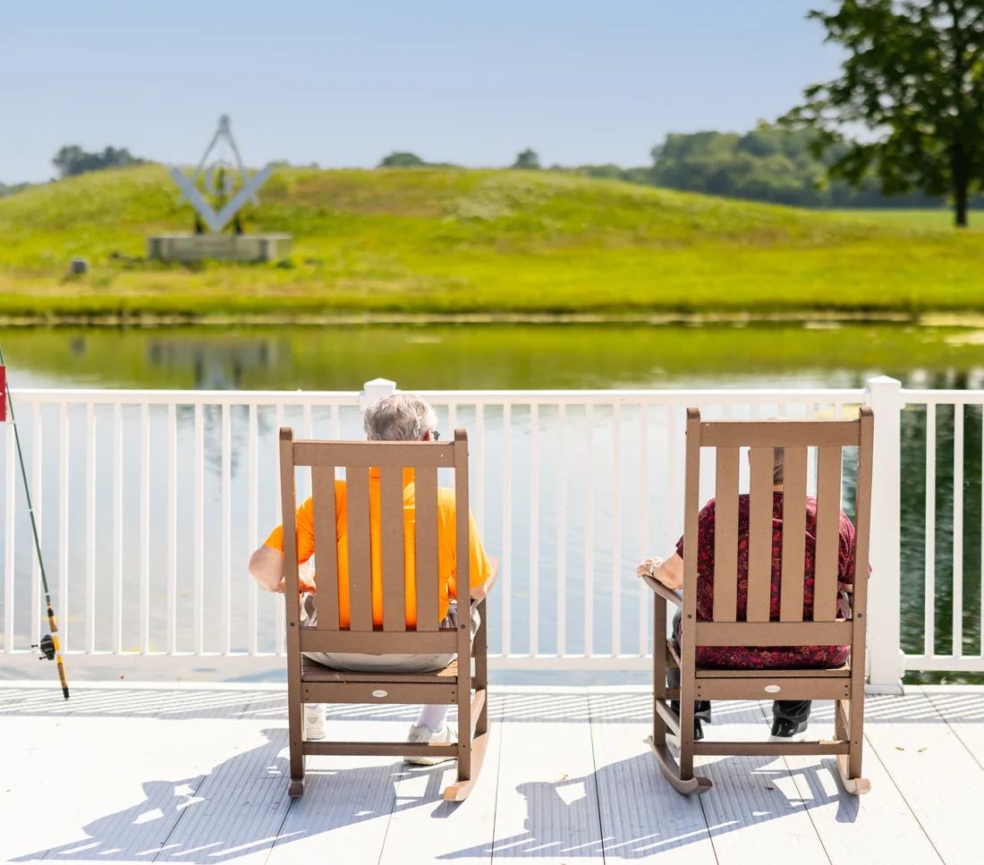 Residents sit in rocking chairs overlooking a pond and grassy hill