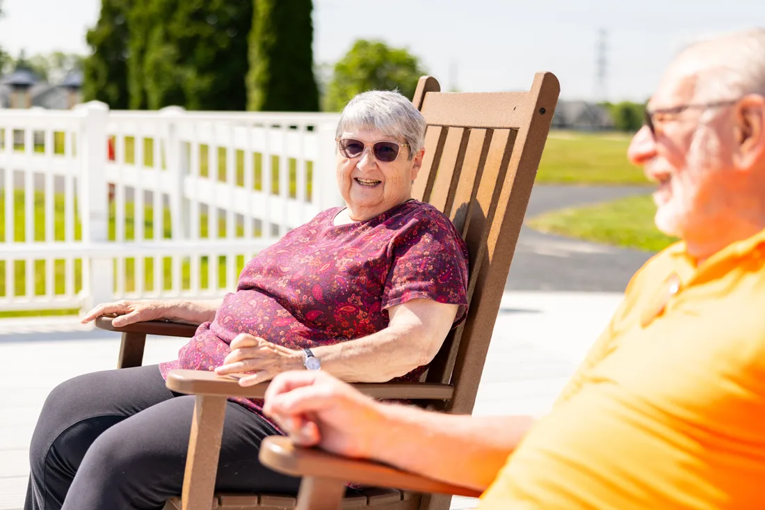Resident male and female sits outside in rocking chairs