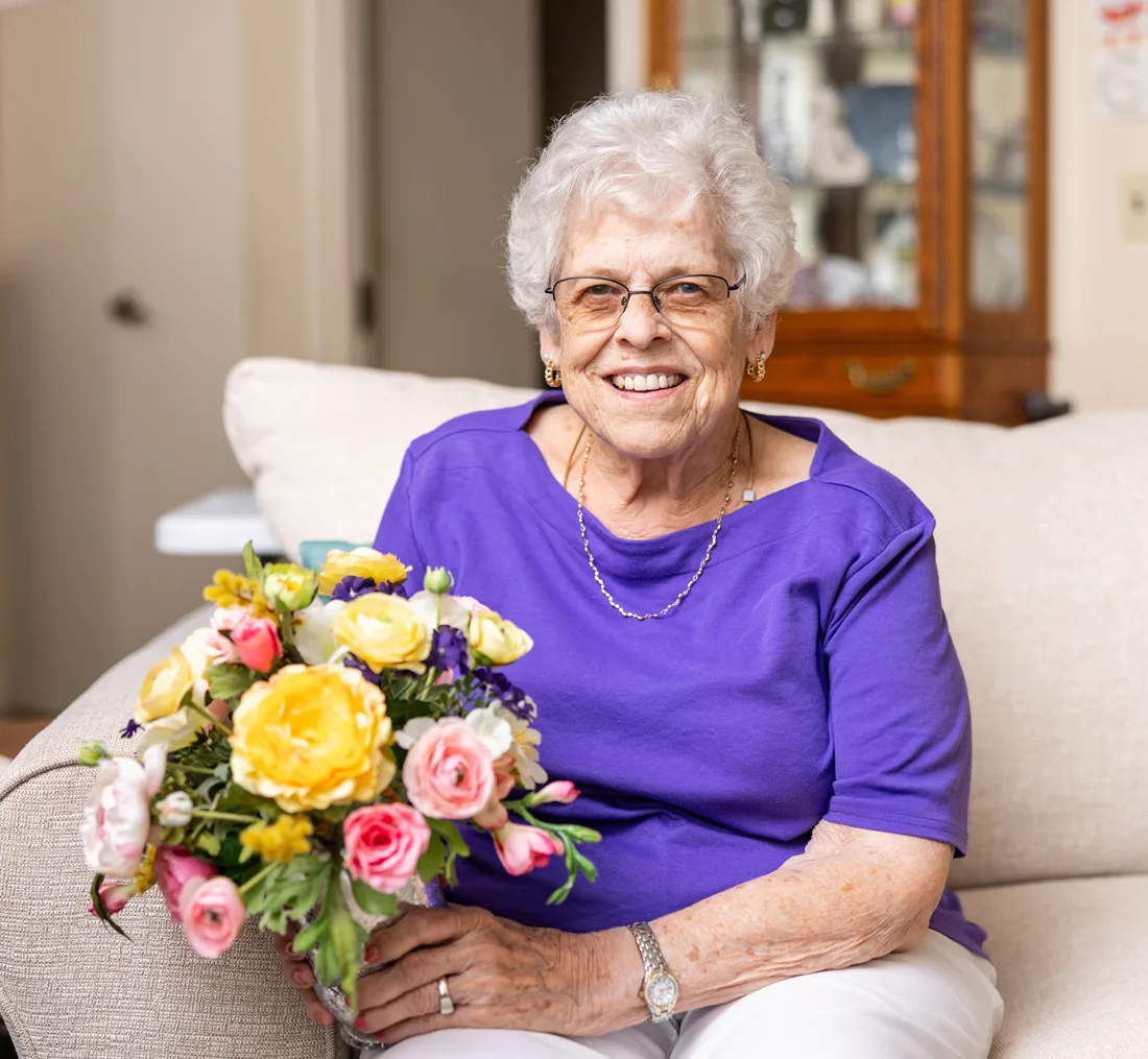 Female older adult holds a bouquet of flowers while sitting on a couch