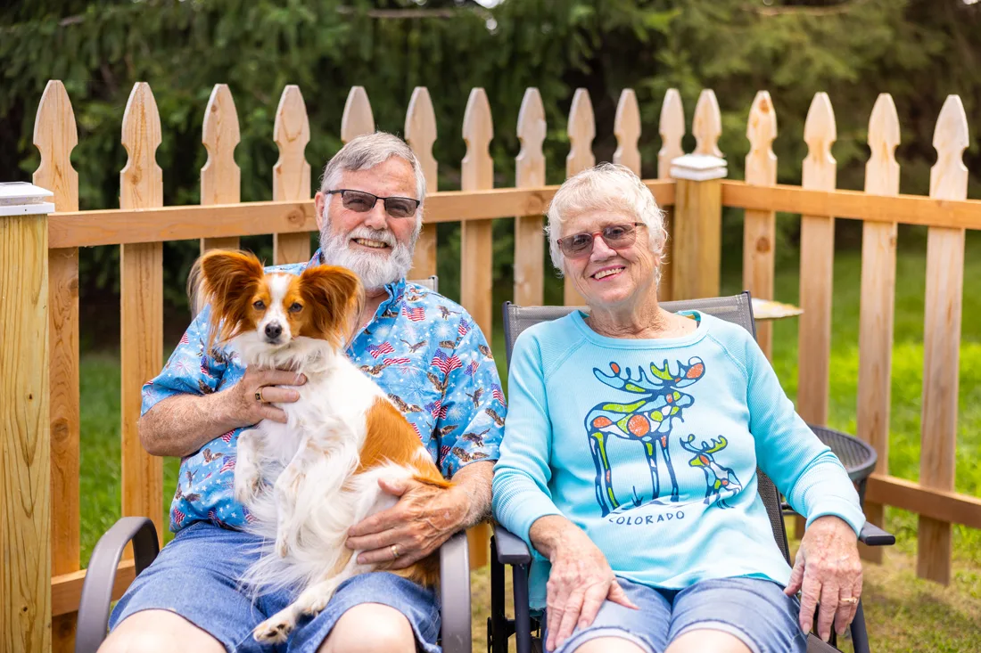 Older adult couple sits outdoors holding a dog