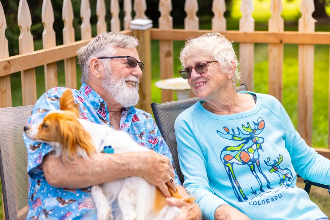 Older adult male and older adult female sit outdoors together with a dog
