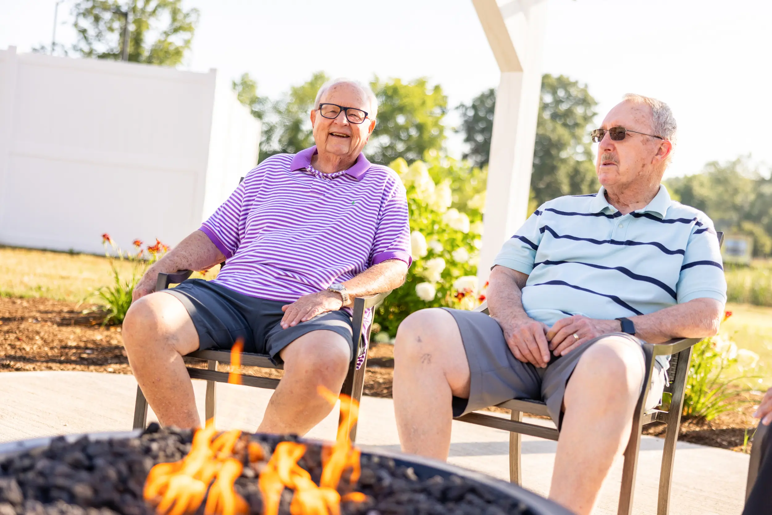 Older adult males sit outside by a firepit