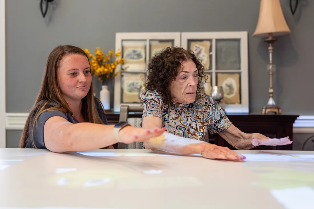 Staff helps older adult female interact with digital images on a large table
