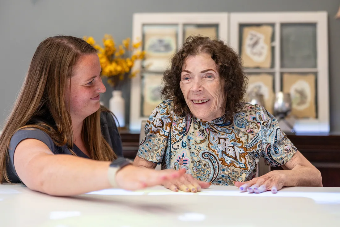 Staff helps older adult female interact with digital images on a large table