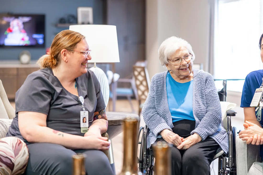 Team members sit and talk with resident in a wheelchair wearing oxygen