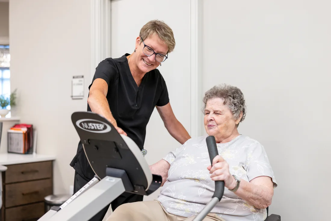 Team member assisting a female resident on exercise equipment