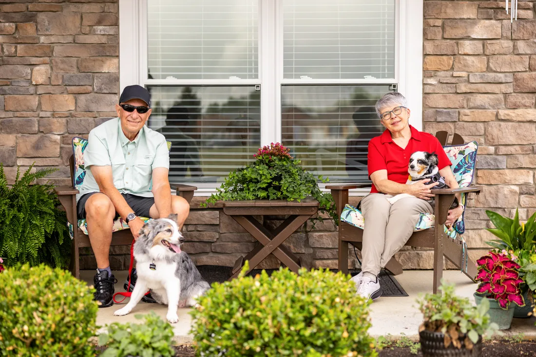 Older adult female and male sitting on the porch with their 2 dogs