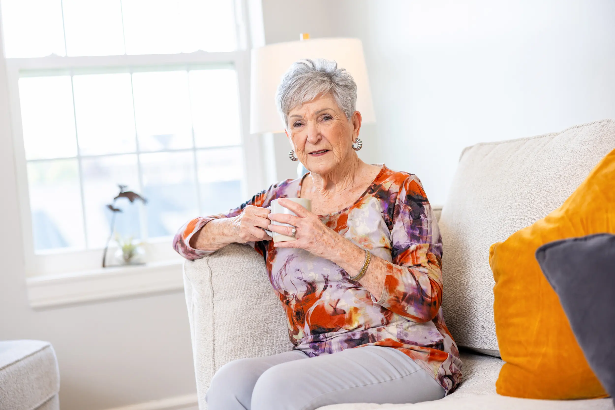 Older adult female holds coffee mug while seated on a couch