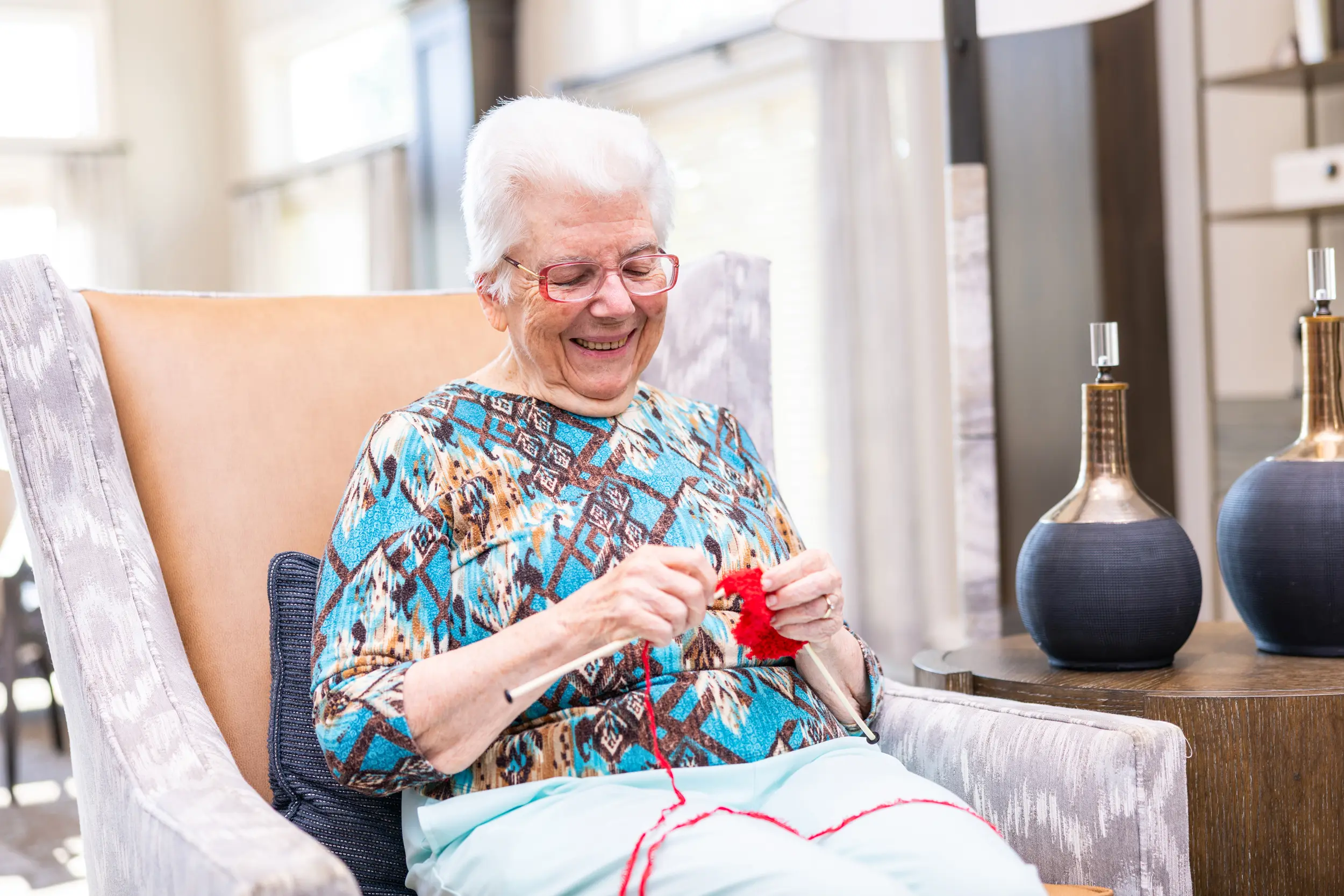 Older adult female sits and knits or crochets with yarn