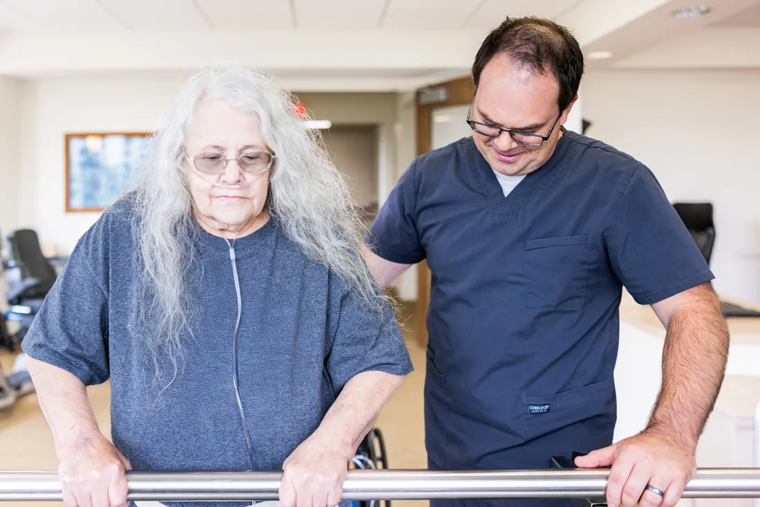 Staff member helps older adult stand using a bar for balance