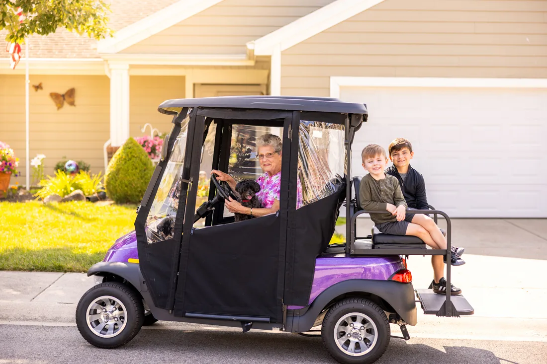 Older adult female with dog on her lap driving a golf cart with 2 young children on the back