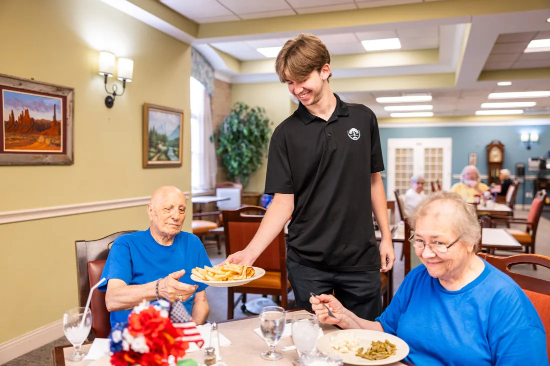 Staff member serving meals to an older adult couple in the dining room
