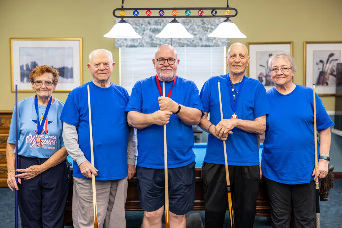 Residents wearing blue shirts hold pool sticks in front of a pool table