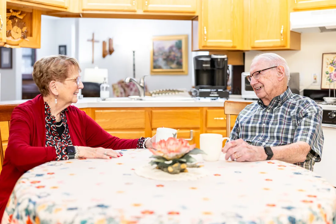 Older adult male and female smiling while seated at a kitchen table
