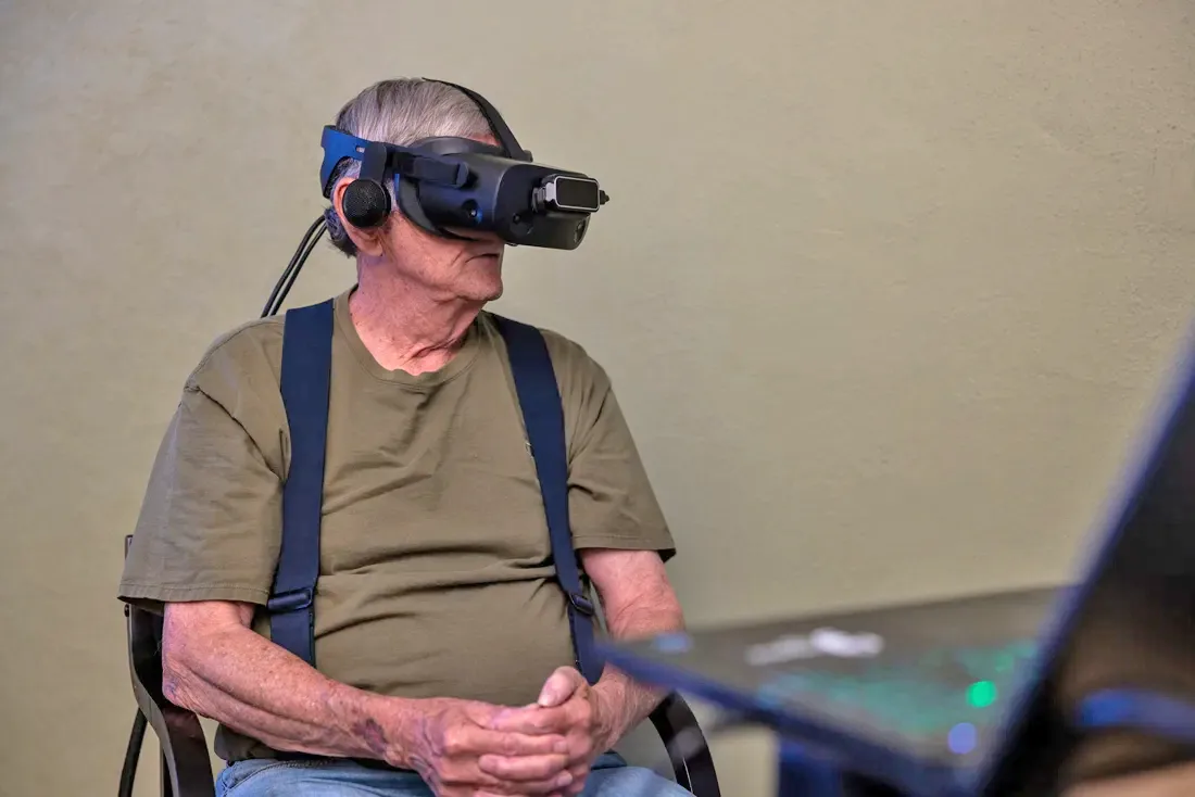 Older adult male uses virtual reality headset while sitting in a chair