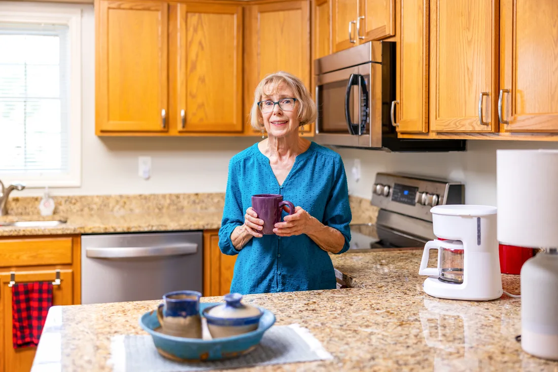 Older adult female holds a coffee cup while standing in the kitchen
