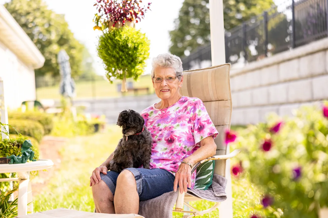 Older adult female holds a dog on her lap while sitting outdoors
