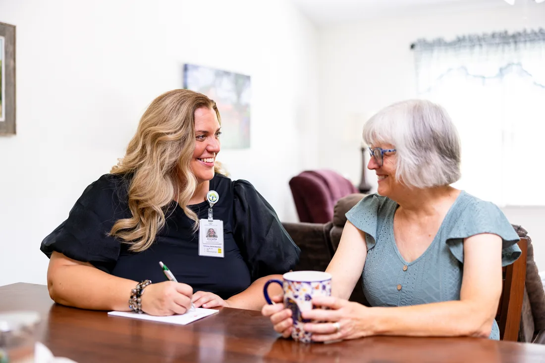 Older adult female holds a coffee cup and talks to an adult female staff member