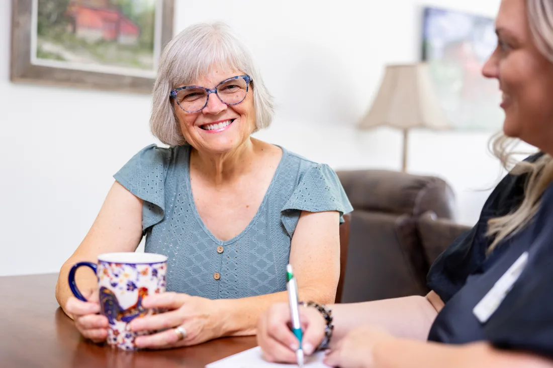 Older adult female holds a coffee cup and talks to an adult female staff member
