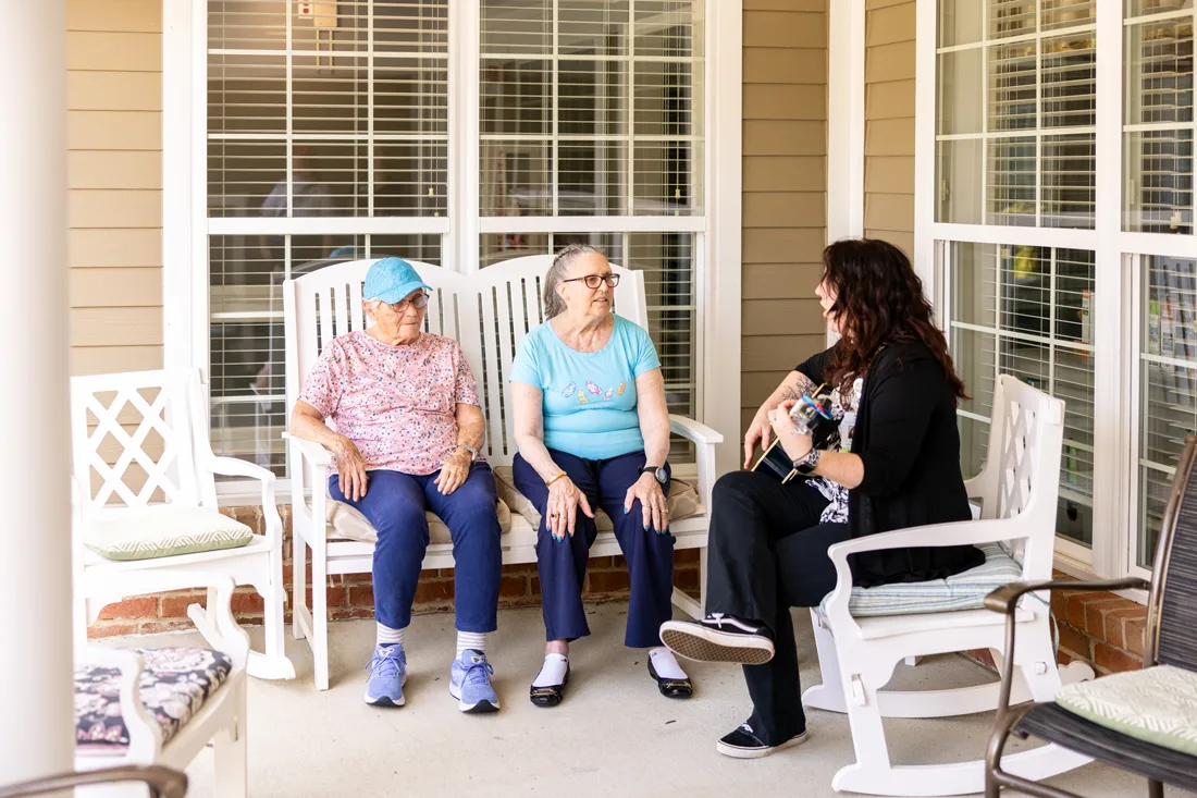 Older adult females sit outside listening to a young female play a guitar