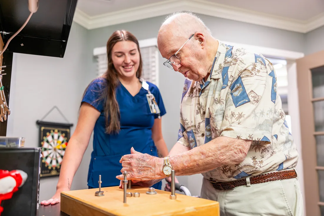 Older adult male puts nuts and bolts together as a female staff member looks on