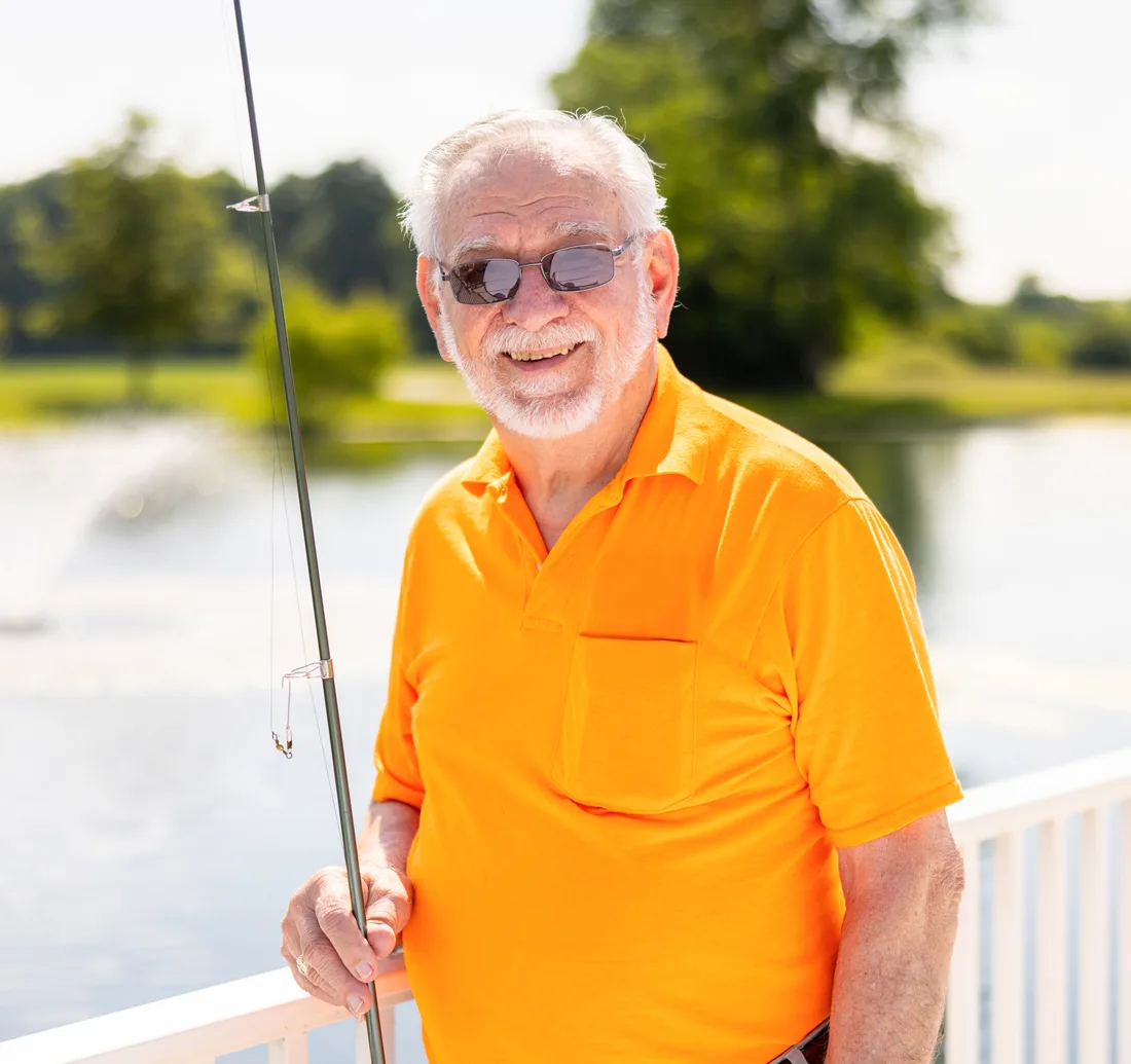 Older adult male holds a fishing pole while standing by a pond
