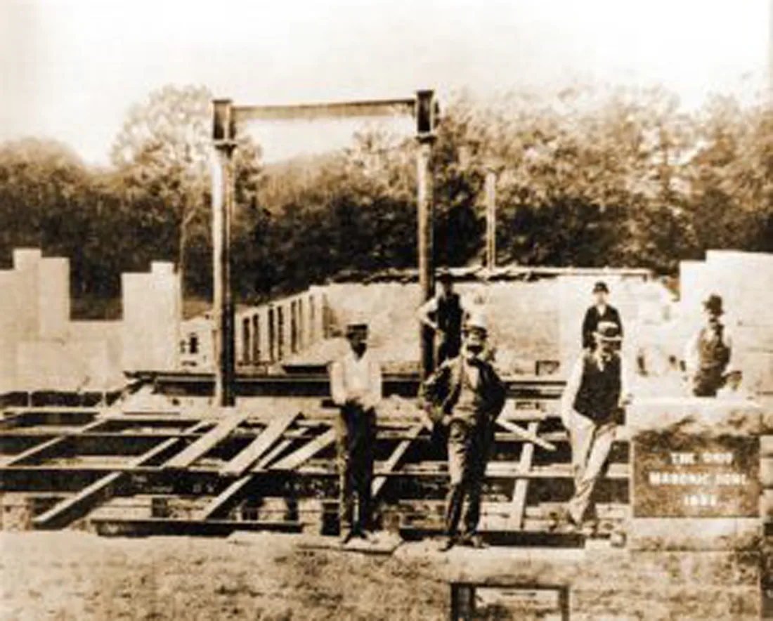 Black and white historical image of men wearing hats standing by building construction