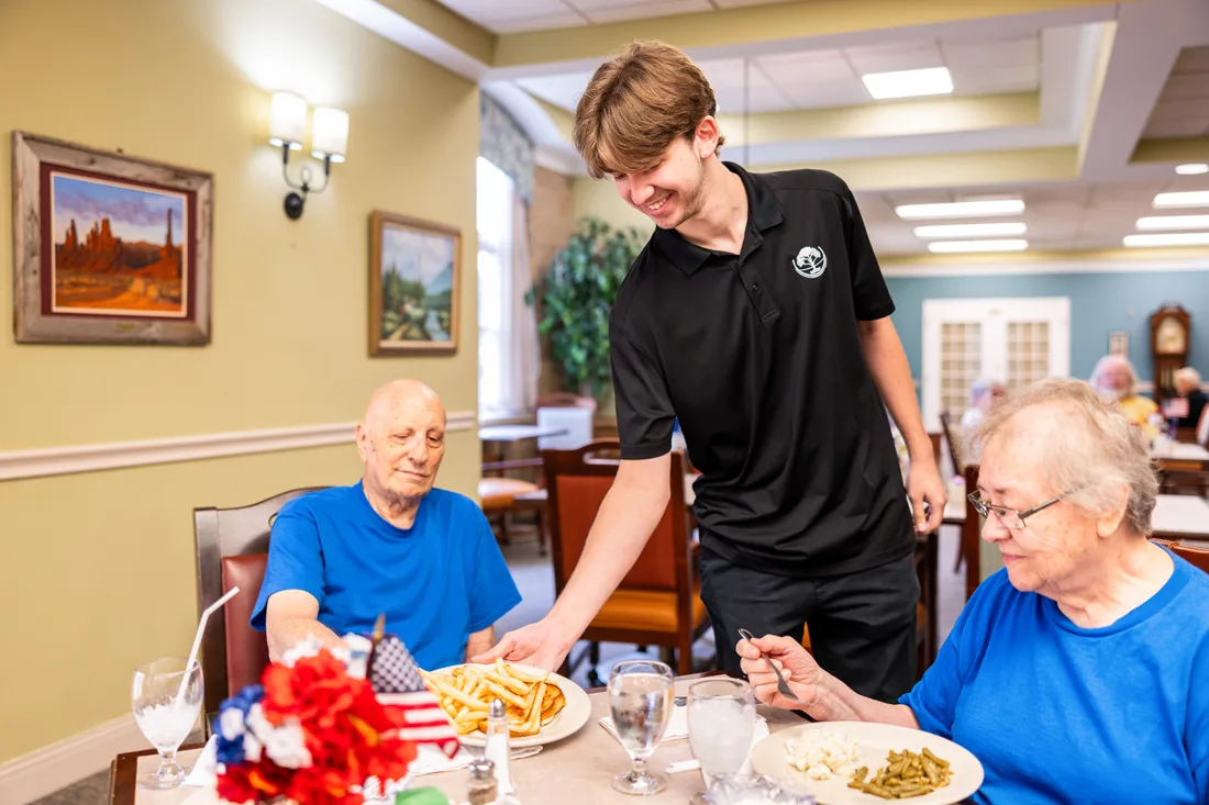Male dining staff member serves residents in the dining room