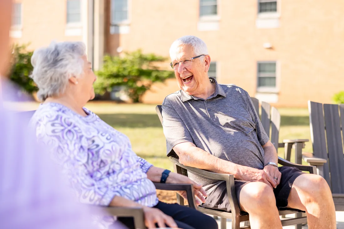 Older adult male and female sit outside laughing and talking