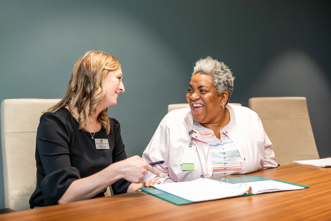 Female staff members talk and review documents in a binder