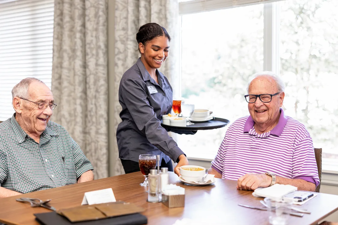 Female dining staff member serves male residents in the dining room