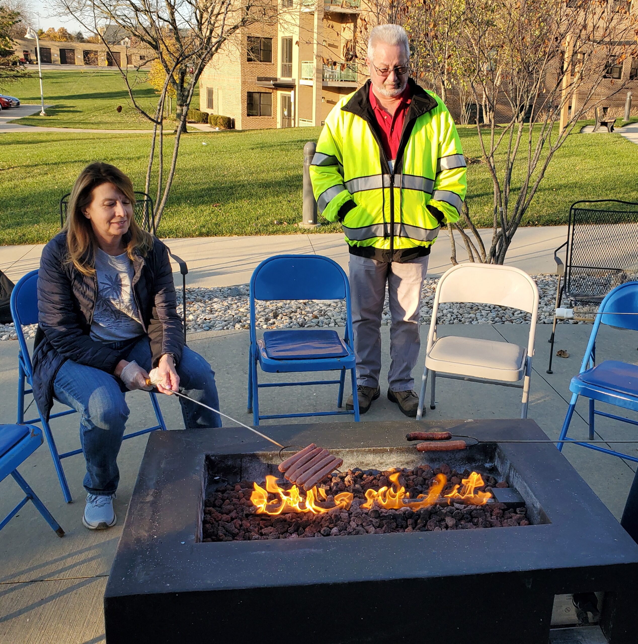 Adults roast hot dogs over a fire outside the community