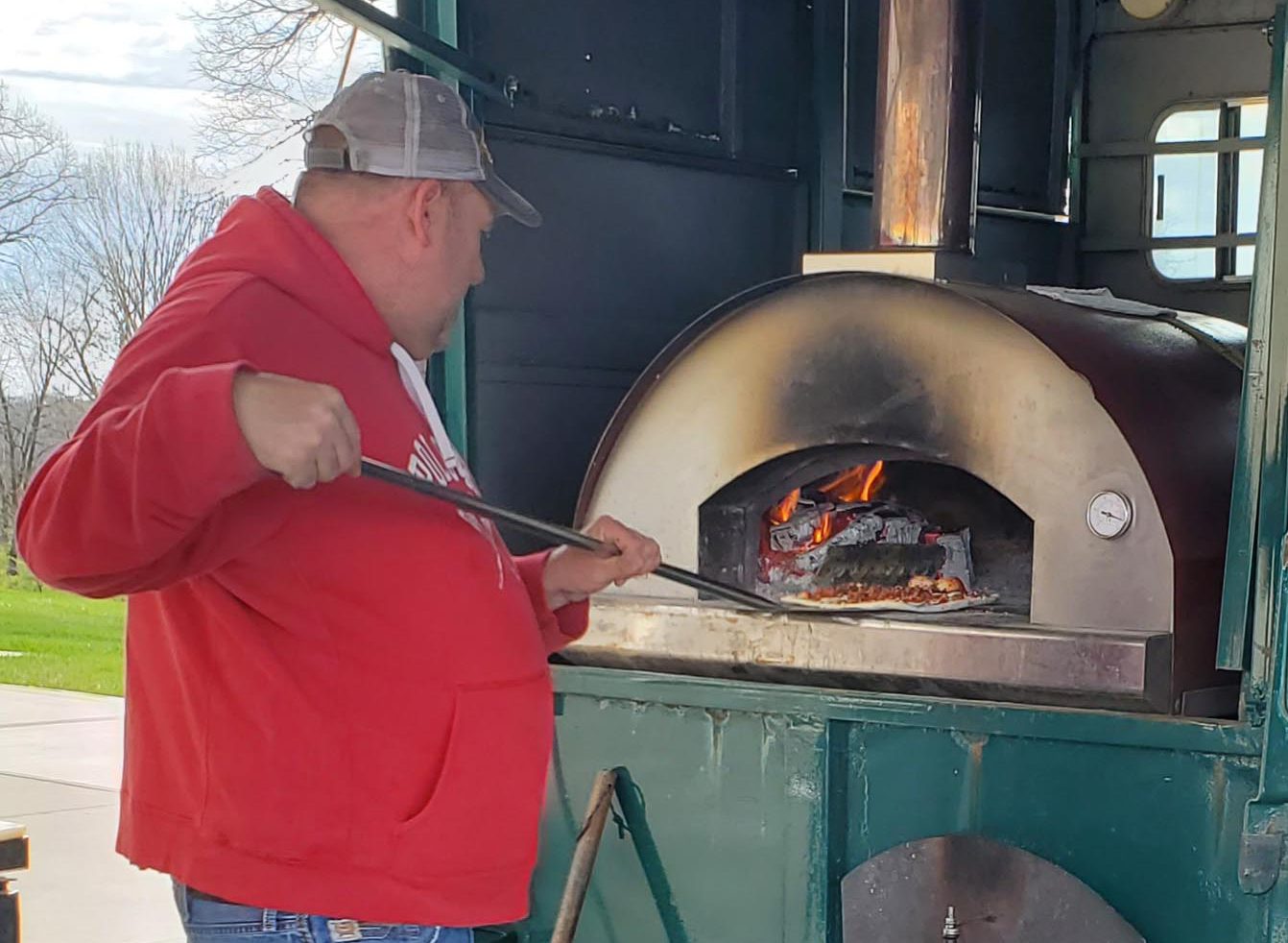 Man bakes pizza in a wood-fired oven outdoors