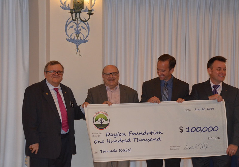 Adult men wearing suits holding a large check to the Dayton Foundation for $100,000