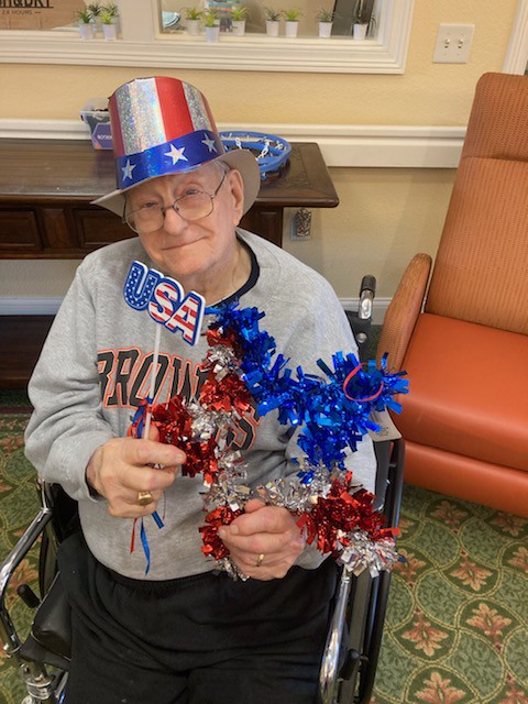 Resident in a wheelchair sits inside wearing patriotic accessories