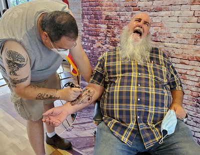 Older adult male gets a tattoo from a male tattoo artist