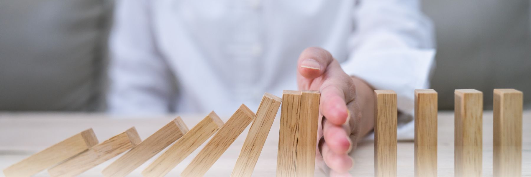 Hand stopping wooden dominoes from knocking other dominoes down