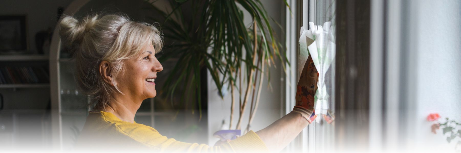 Older adult woman freshening up her space by cleaning her windows while smiling