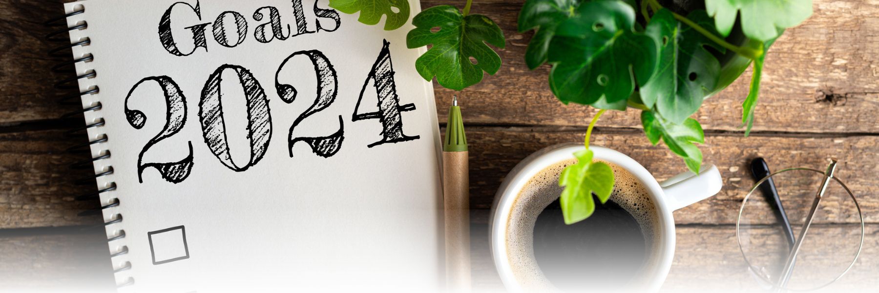 Goals 2024 notebook with a pen, cup of coffee, plant, and eyeglasses