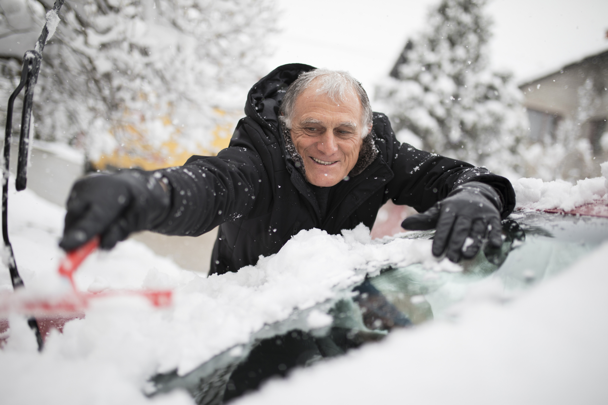 Older adult male scrapes vehicle windshield