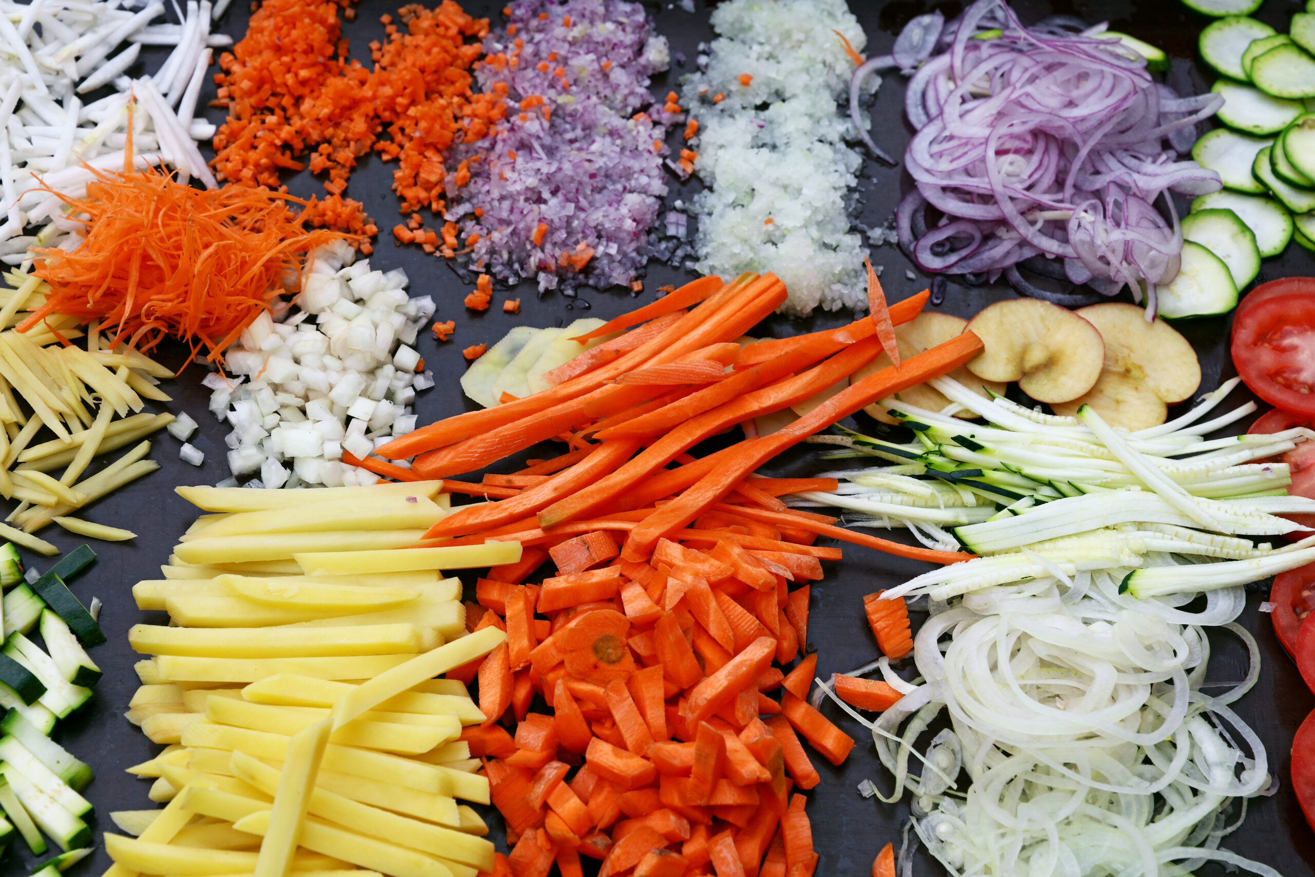 Close up assorted cut and sliced fresh vegetables on black cooking board