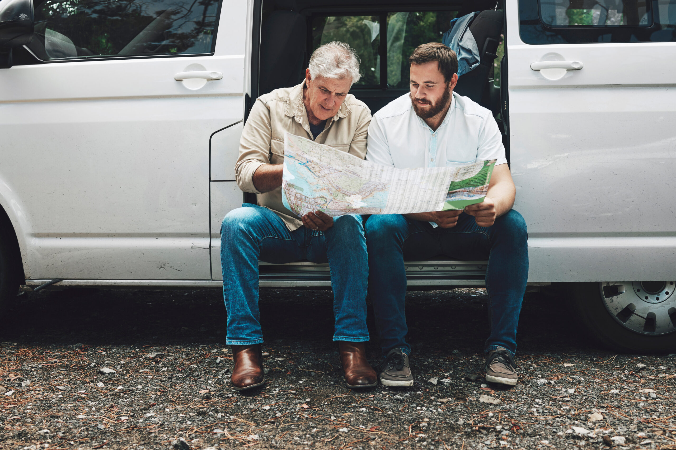 Senior man and adult male with map on travel adventure looking for destination direction in van talking and traveling together