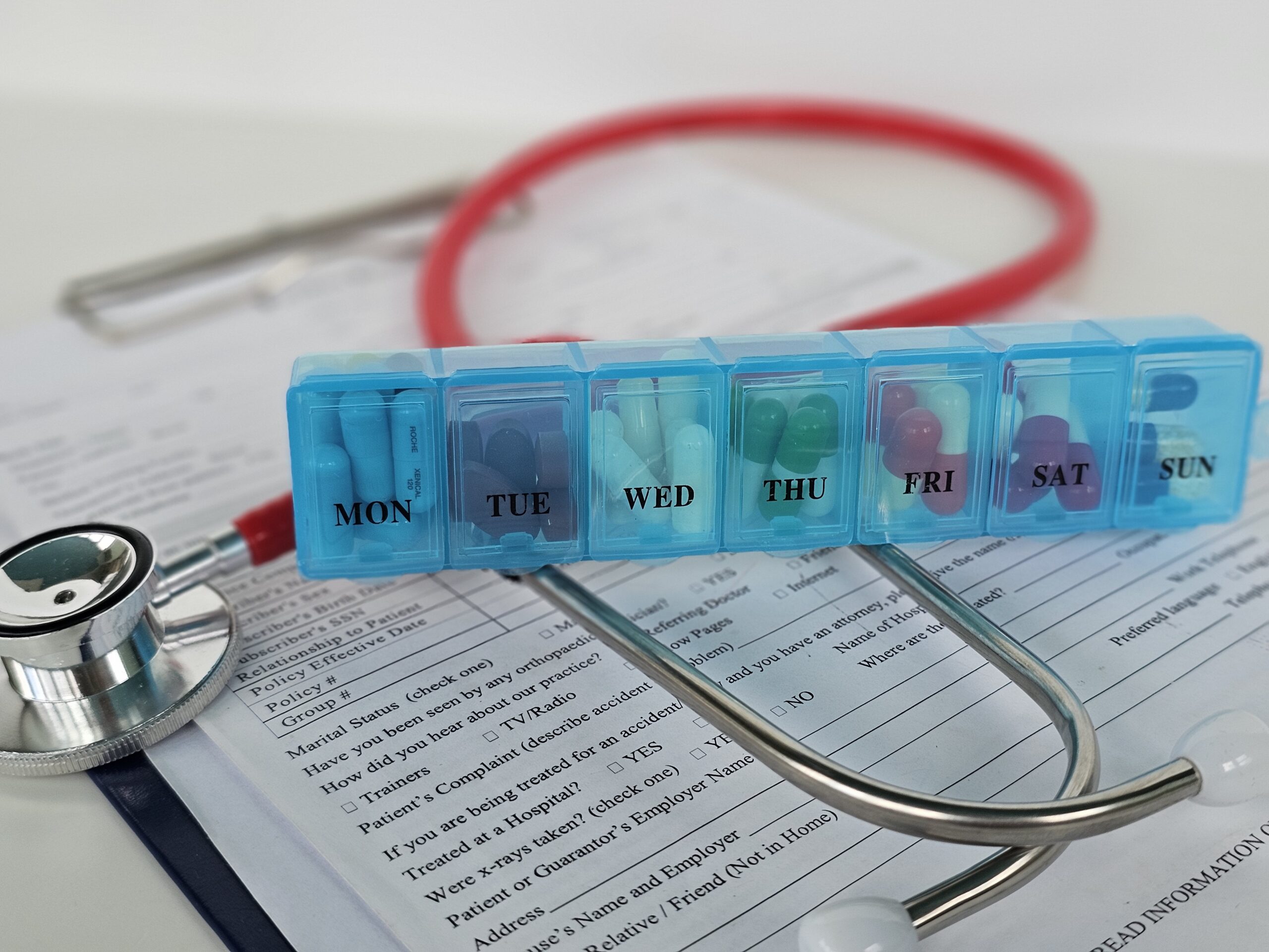 Weekly medication organizer sits on a medical form with a stethoscope