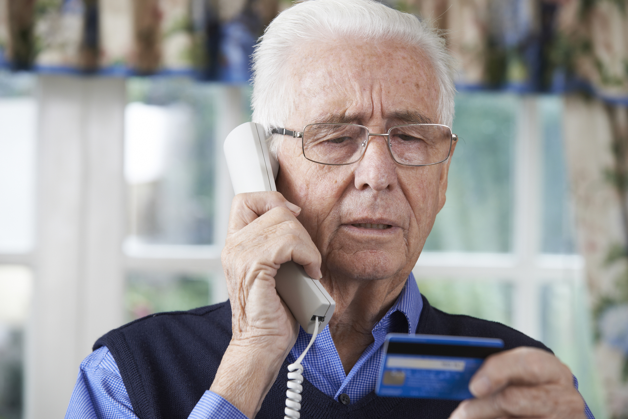 Older adult male holds a landline phone while looking at a credit card