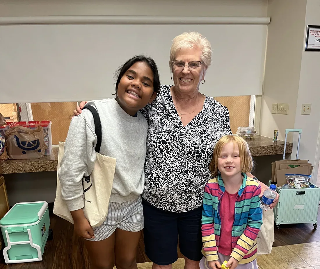 Older adult female stands and smiles beside two young girls