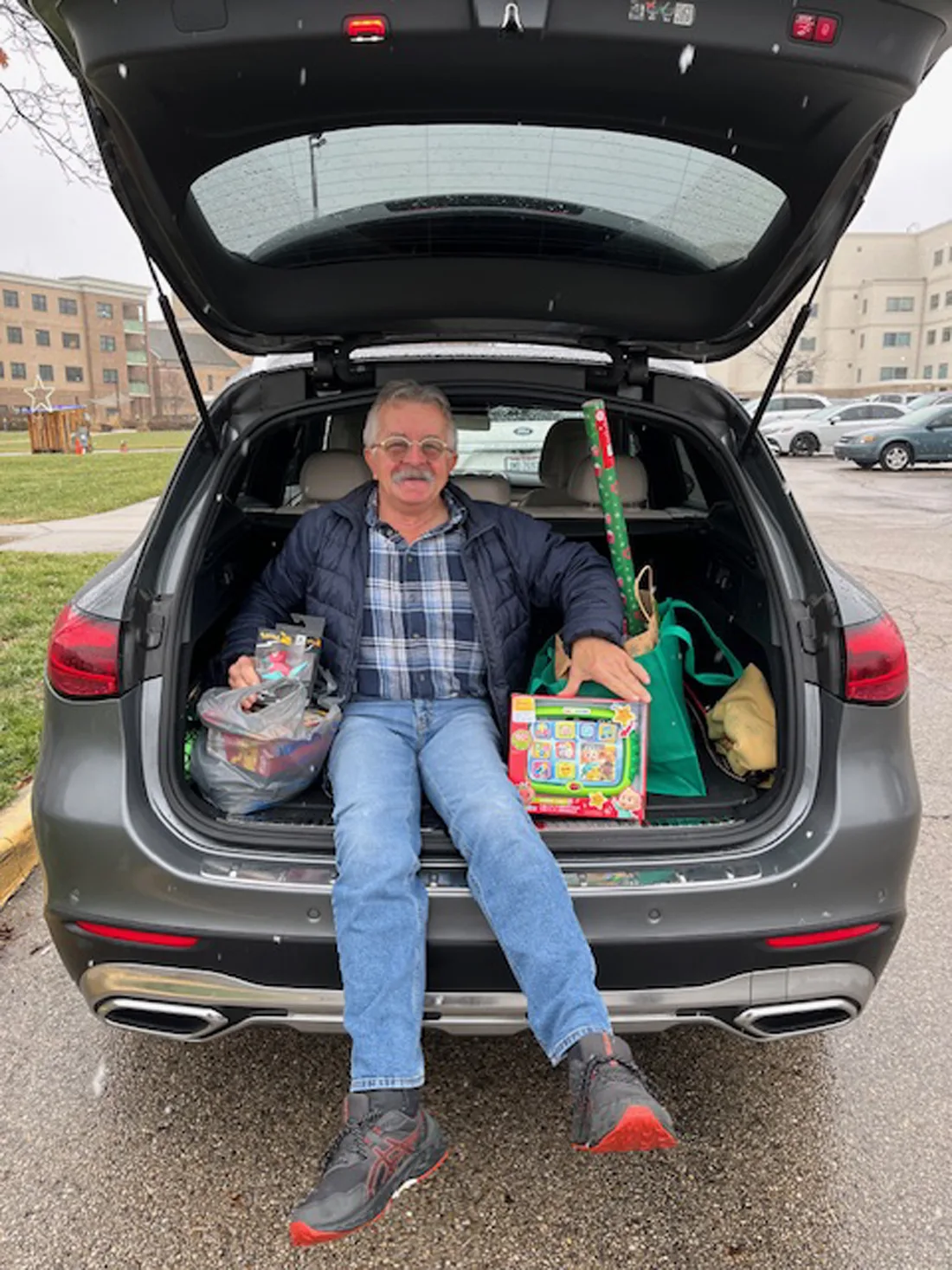 Adult male sitting in back of a vehicle next to holiday gifts and wrapping paper