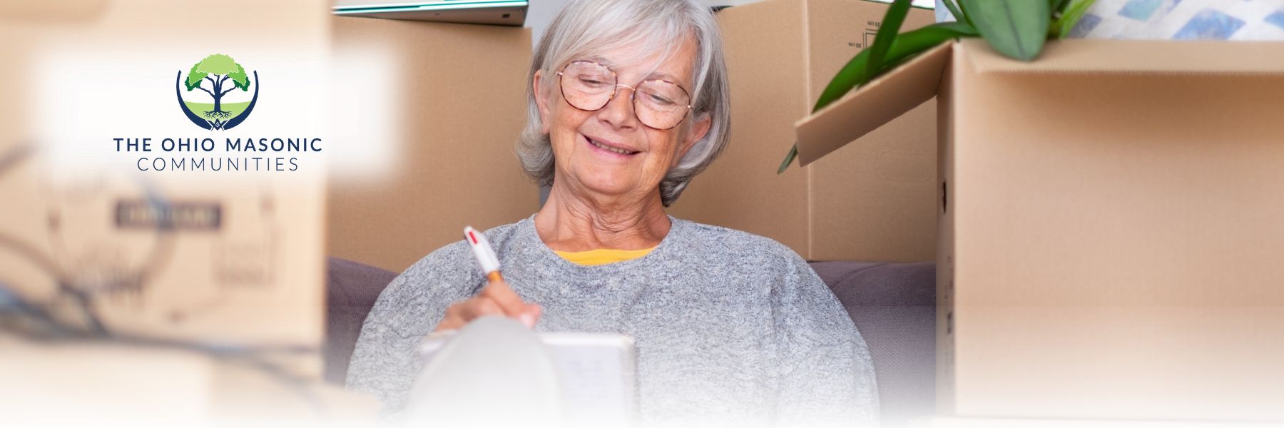 Older adult female writes on a notebook and is surrounded by boxes